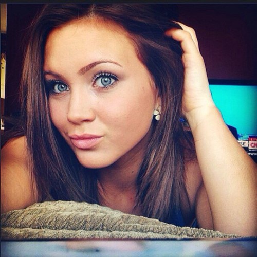 A young woman with striking blue eyes and brown hair poses for a selfie.