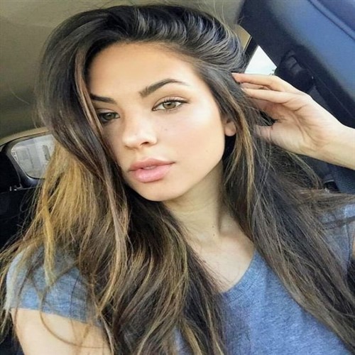 A young woman with long, wavy brown hair and light skin.