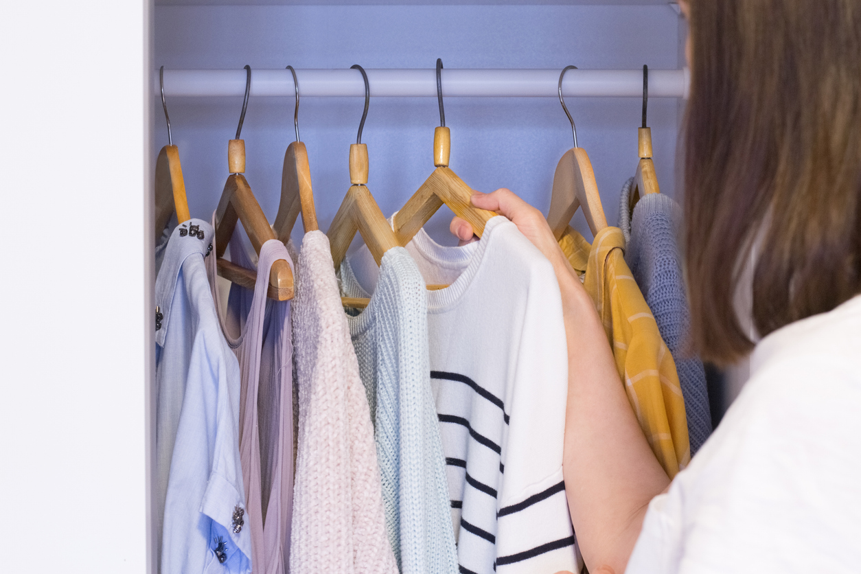 A person is choosing clothes from a closet with wooden hangers.