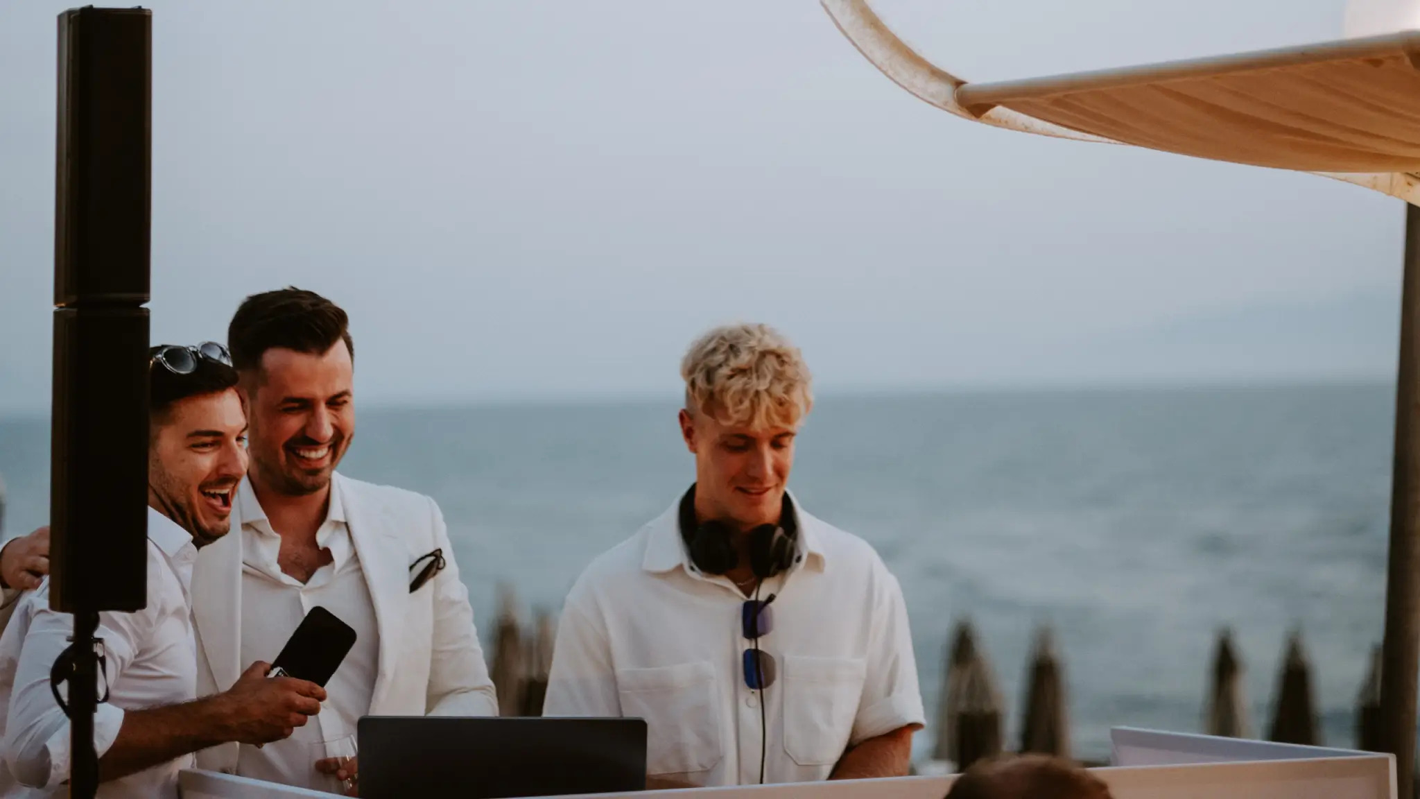 Zwei fröhliche Personen mit Hochzeits DJ Nathan White am Strand beim DJ-Pult