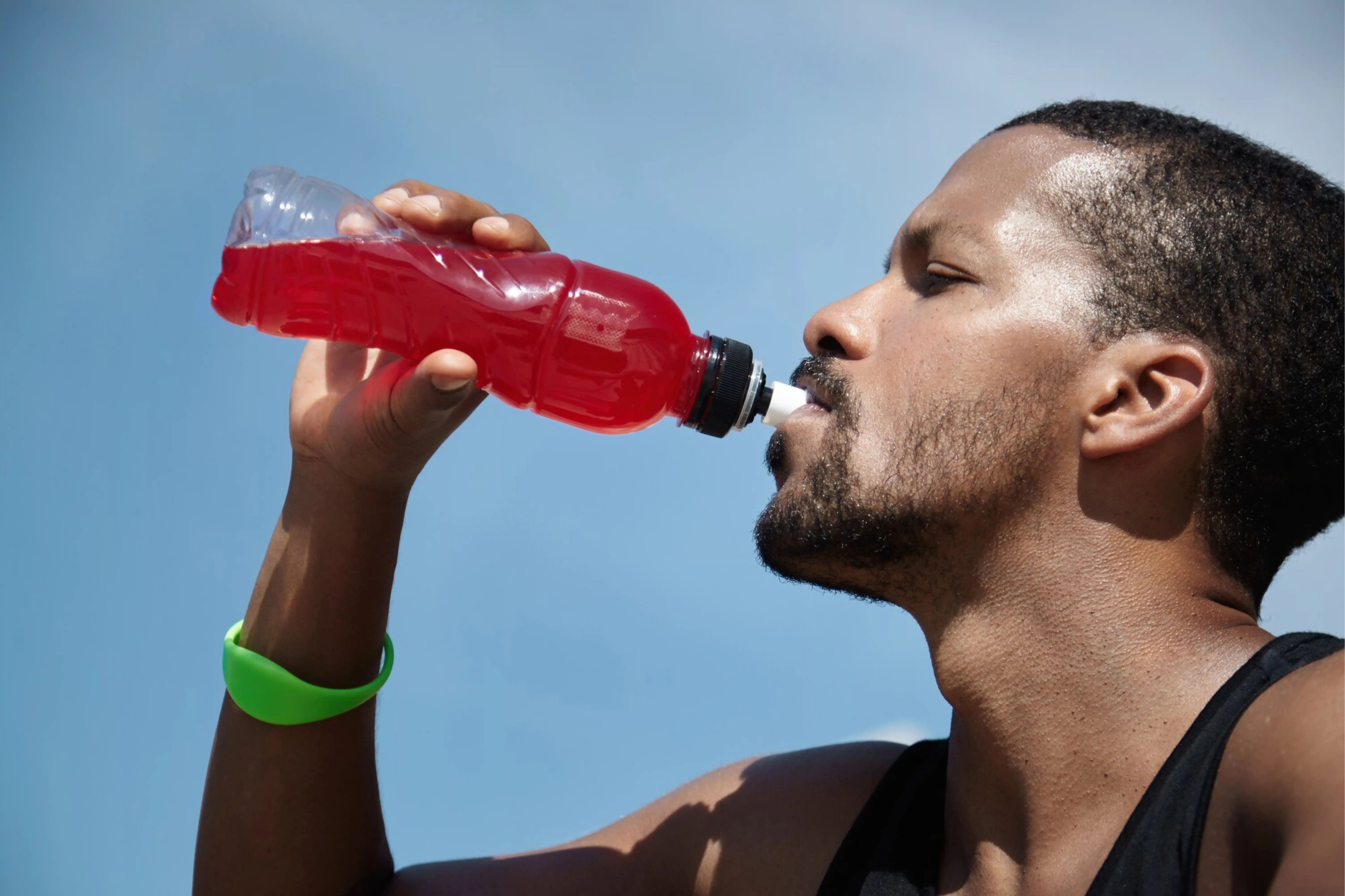Hombre bebiendo agua de hibisco de una botella deportiva contra un cielo azul.