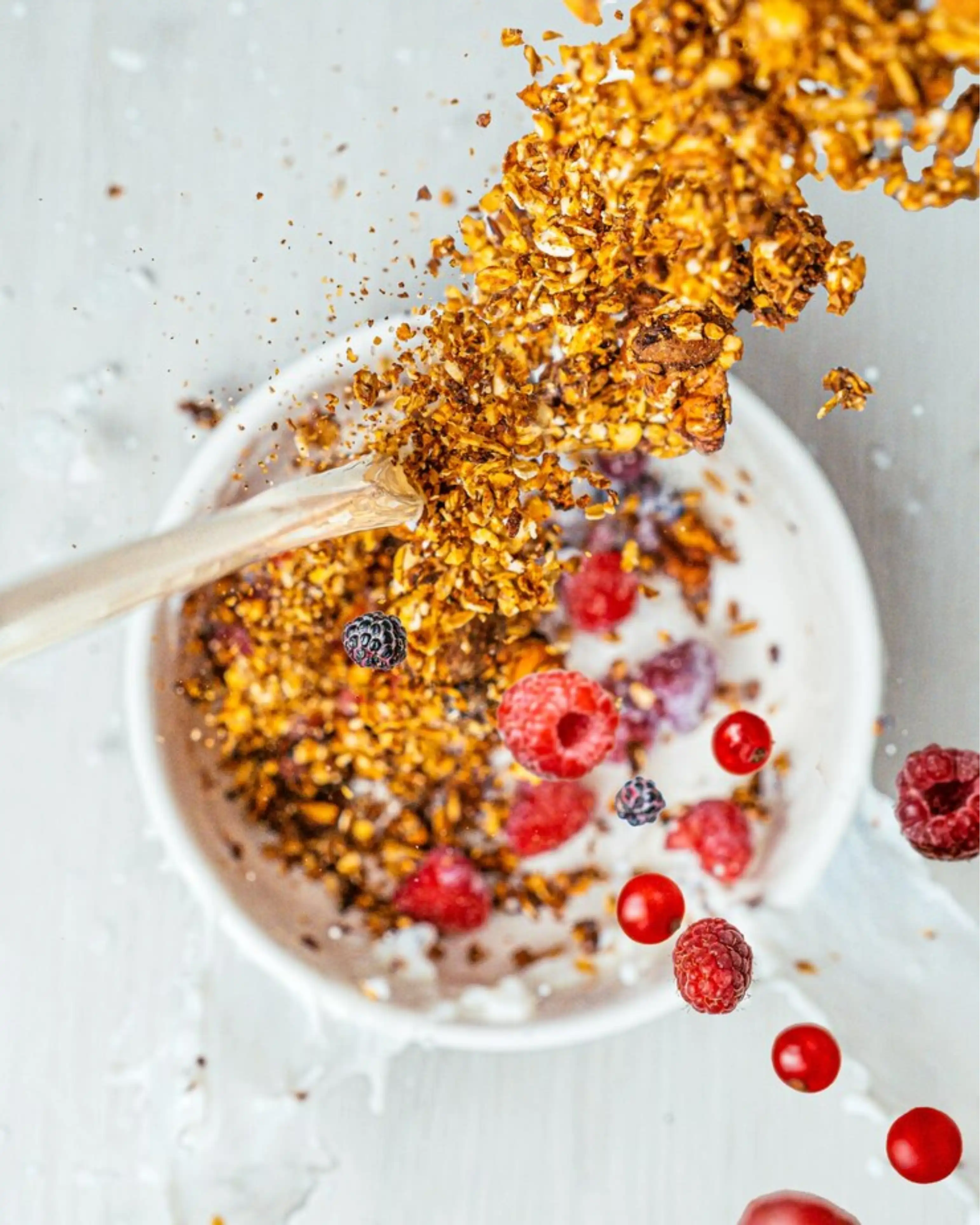 Granola and berries being added to a bowl of yogurt.