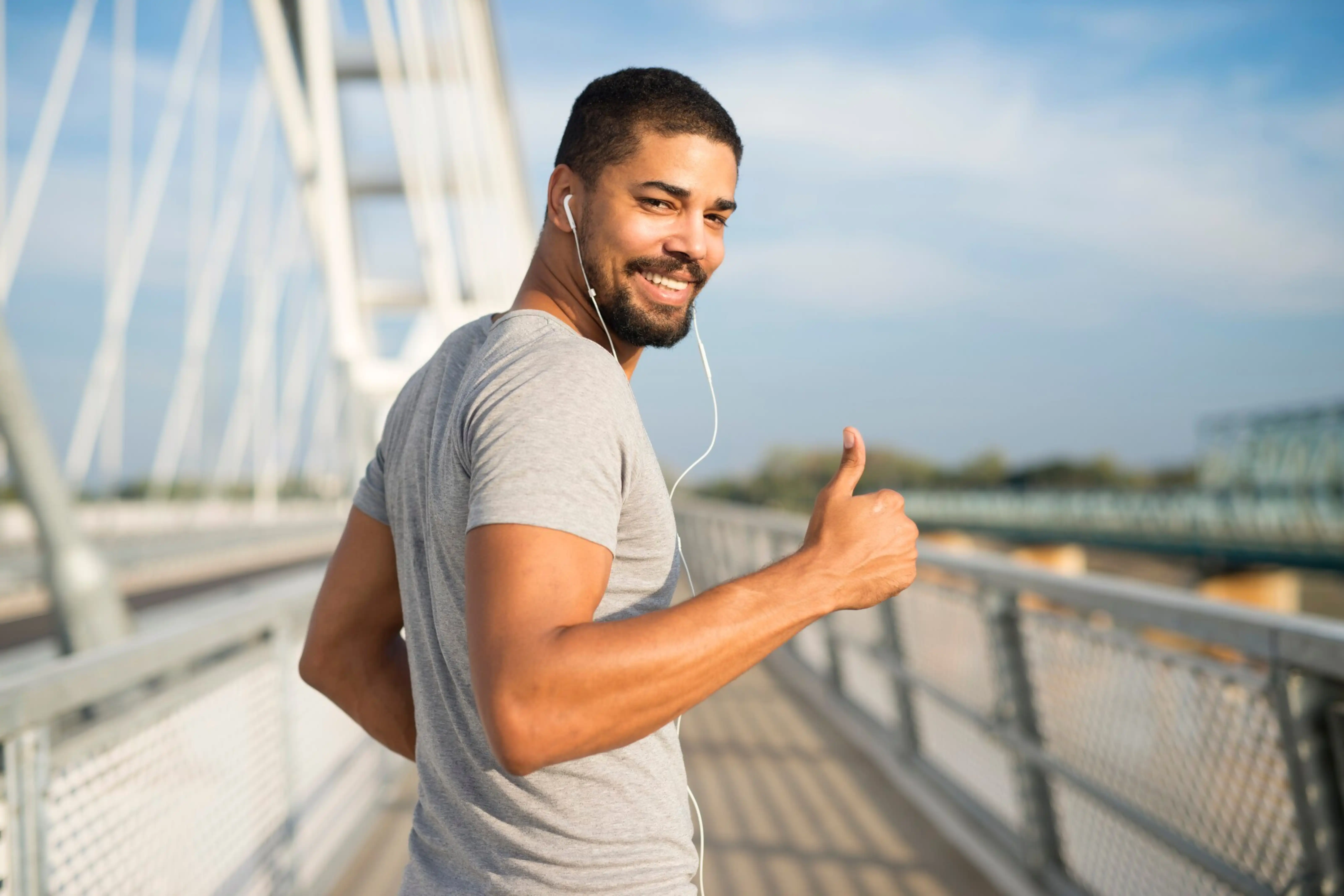 Un hombre sonriente levanta los pulgares mientras camina por un puente.
