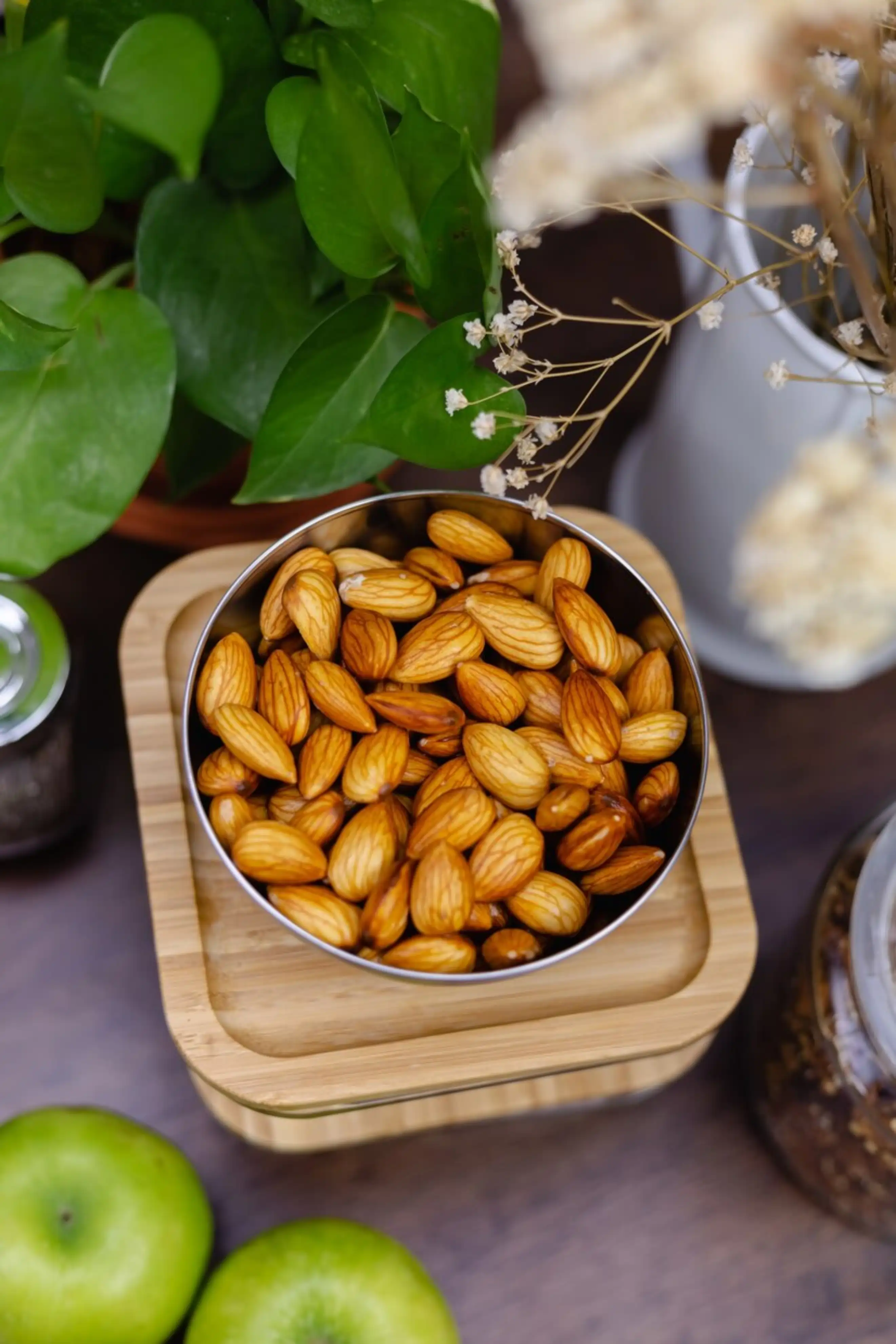 Bowl of almonds surrounded by green plants and decor.