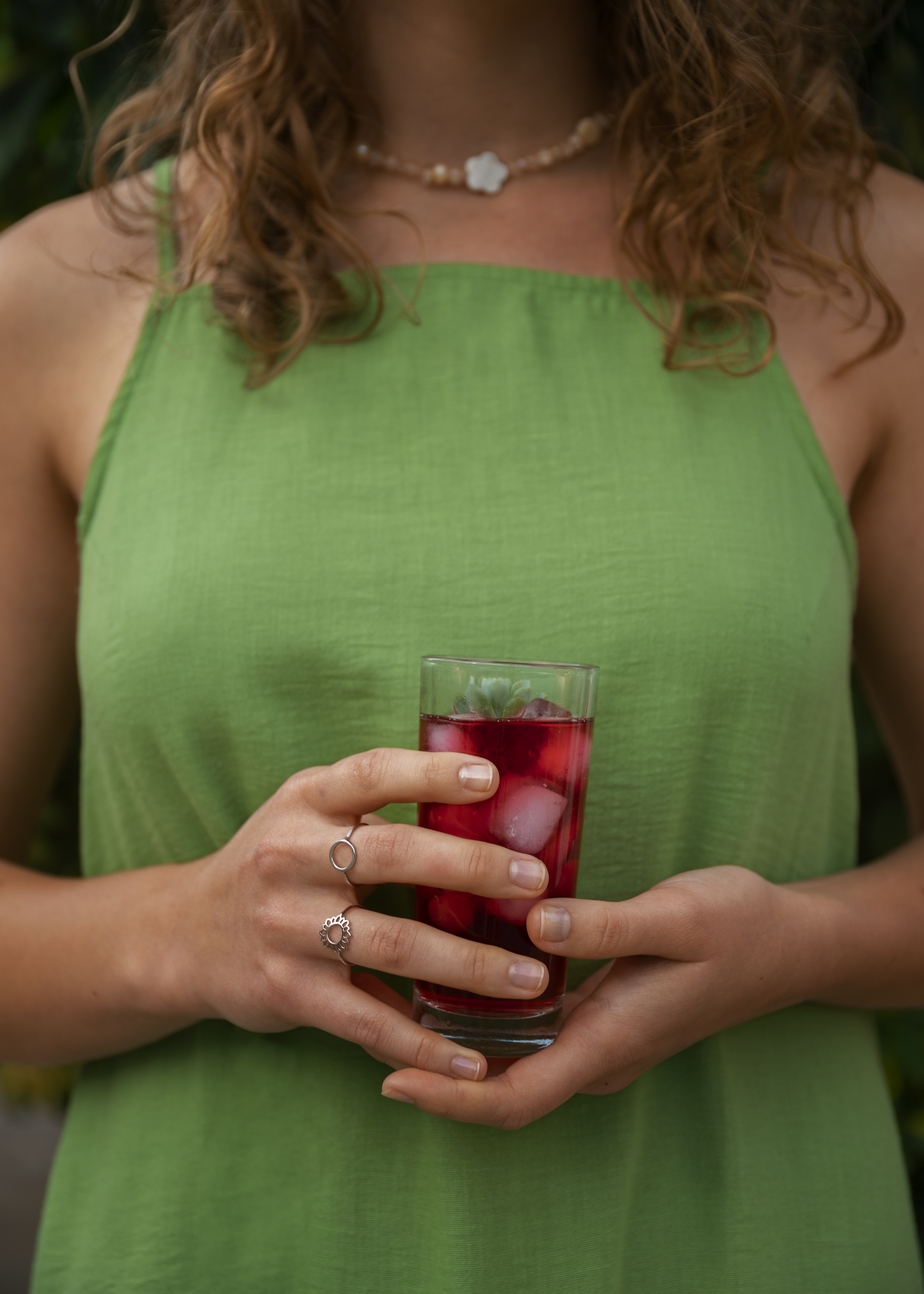 Mujer con vestido verde sosteniendo un vaso de agua de jamaica helada.