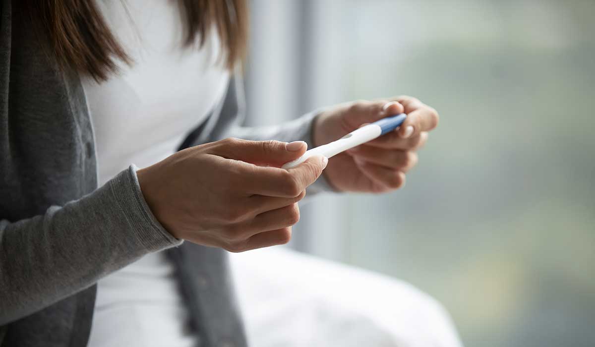 Woman holding a pregnancy test, looking intently at results.