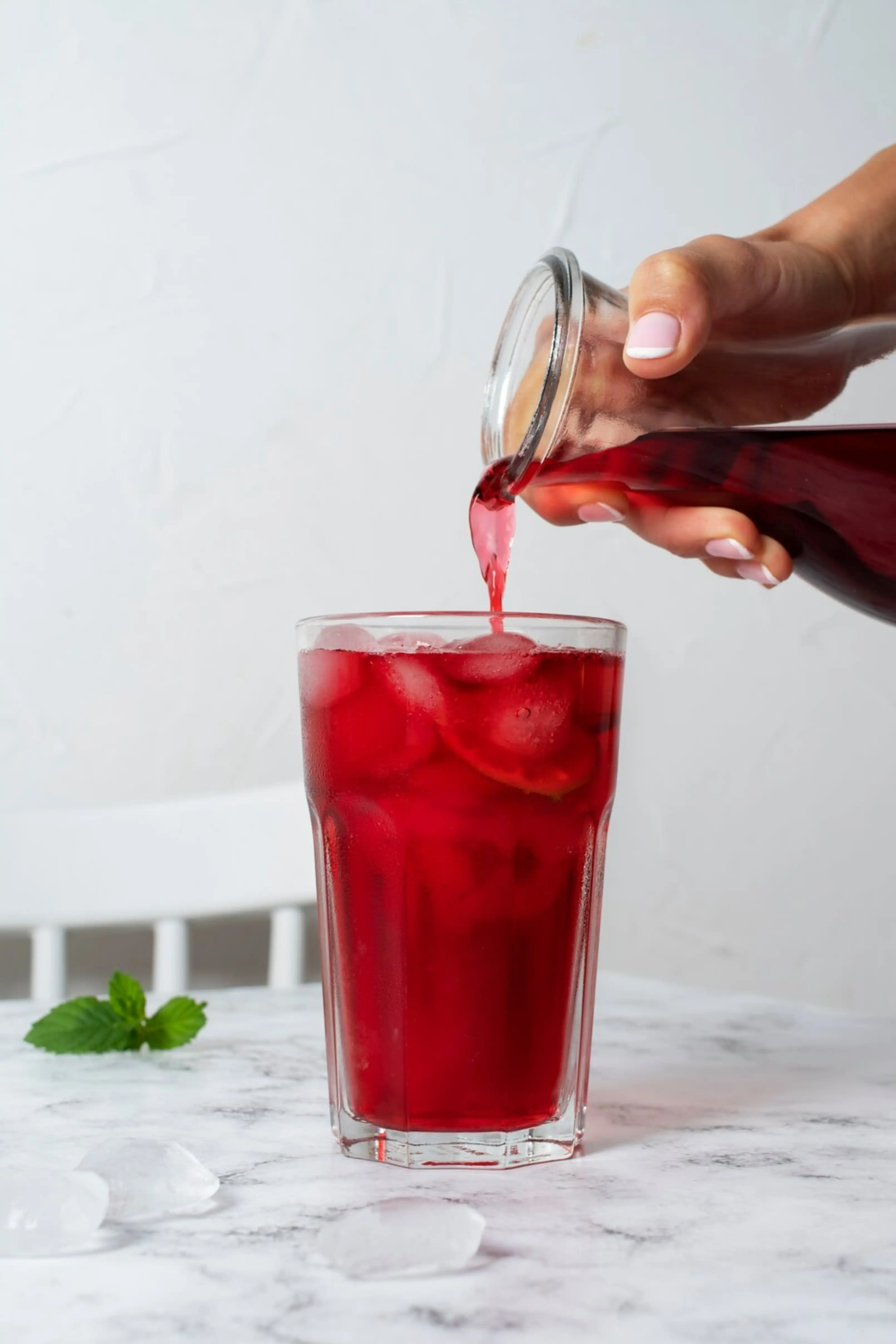 Sirviendo una bebida de hibisco con hielo en un vaso.