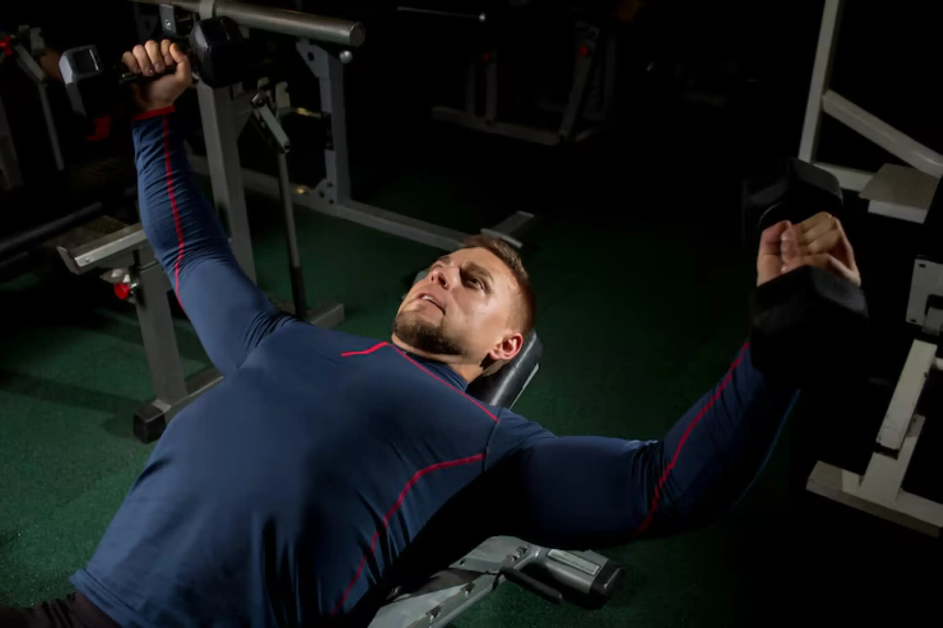 Man exercising with dumbbells on a bench in a gym.