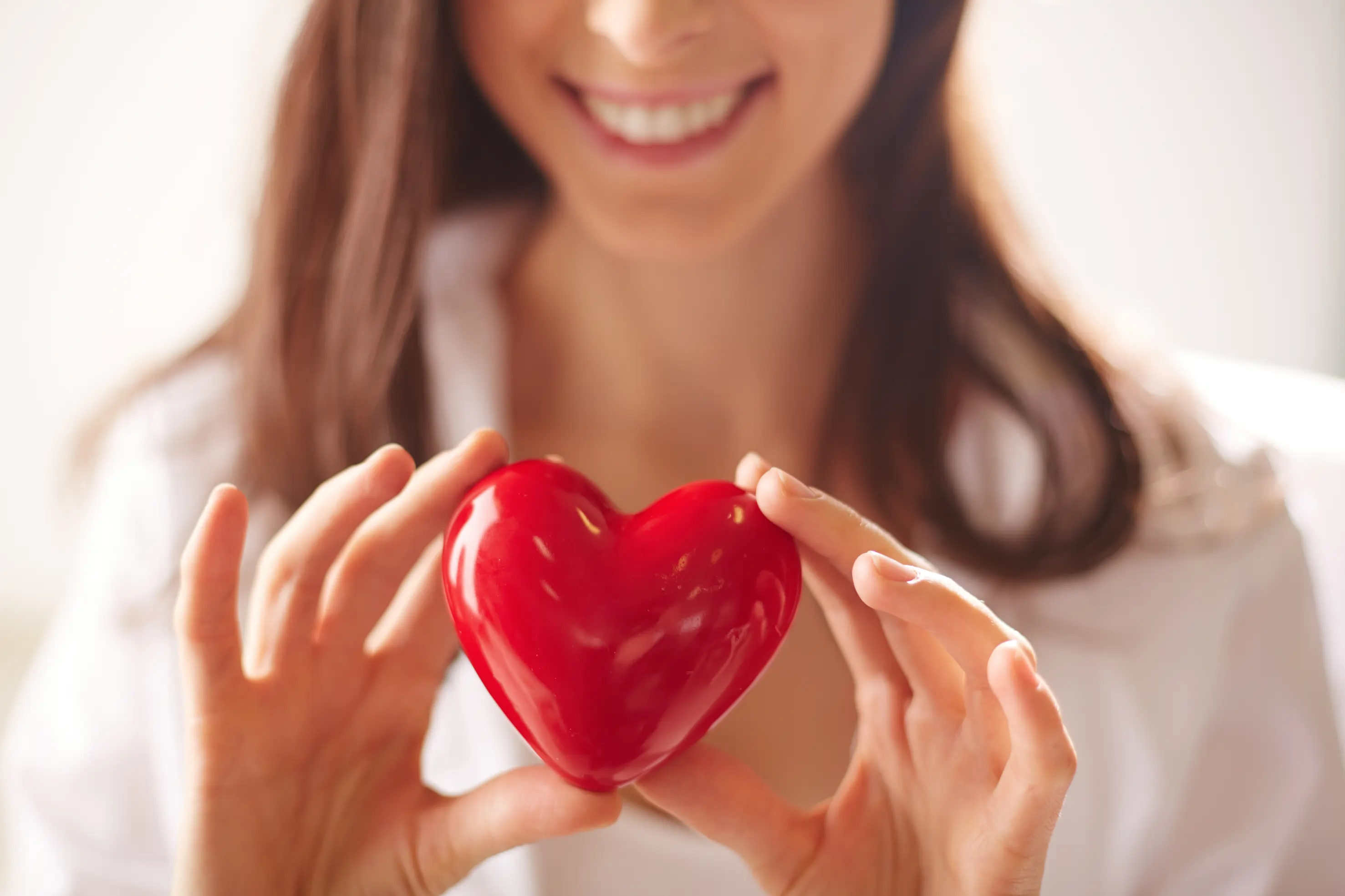 Mujer sonriente que sostiene un corazón rojo brillante en sus manos.