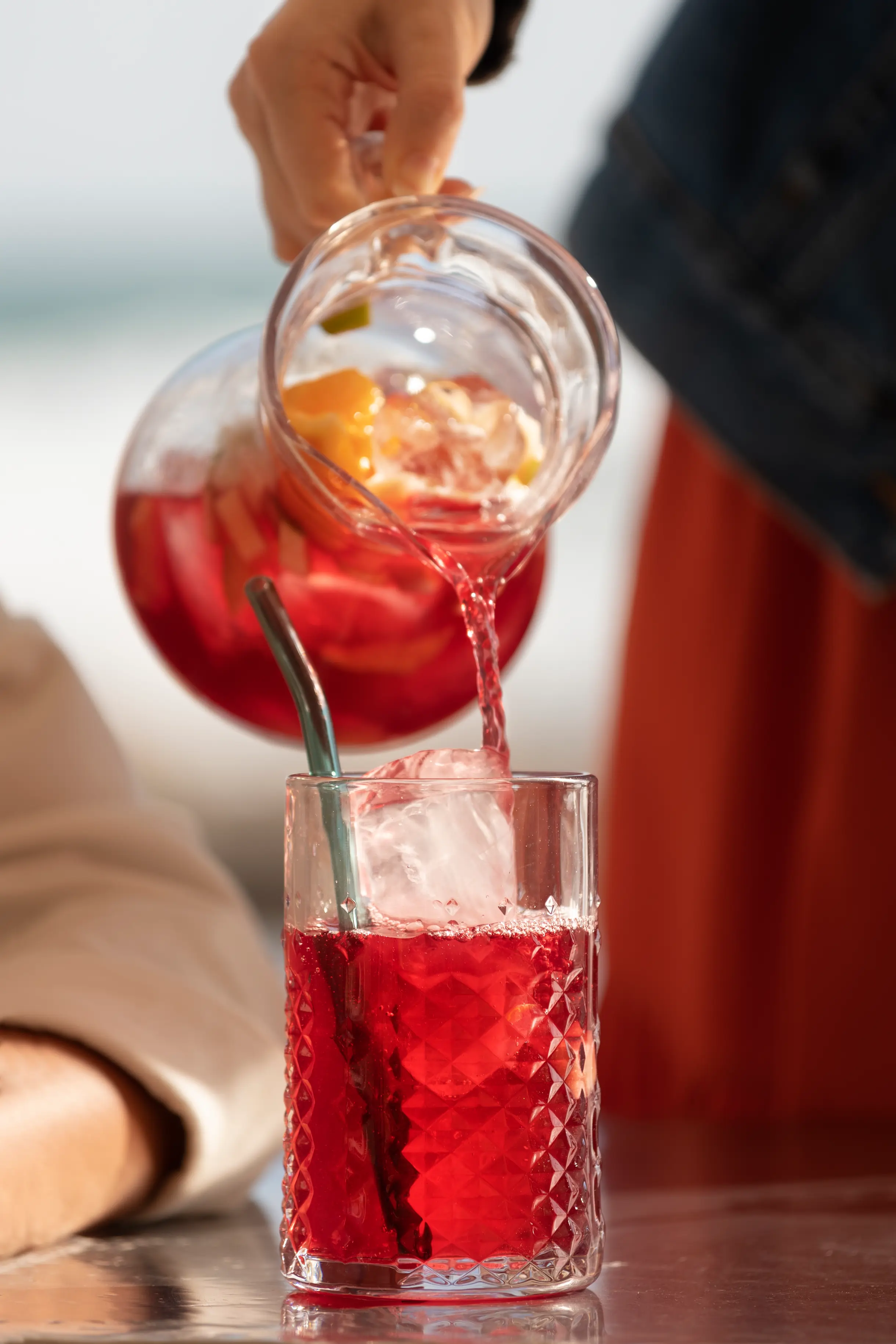 Una mano vierte agua de hibisco de una jarra en un vaso con hielo.
