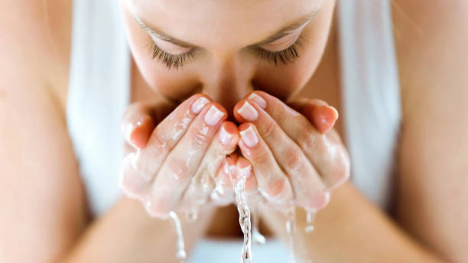 Person washing their face with water in hands.