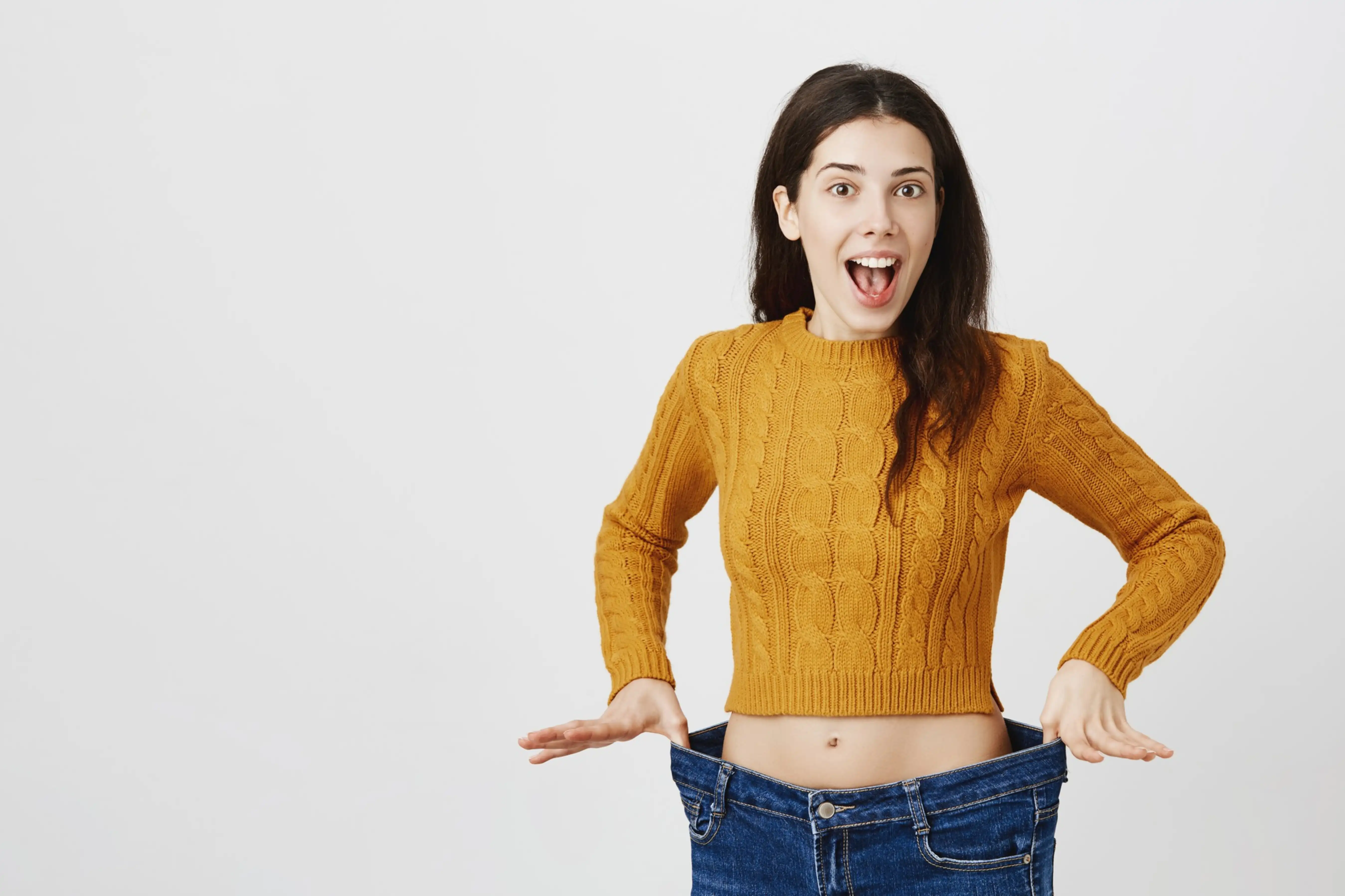 Excited woman showing oversized jeans with a joyful expression.