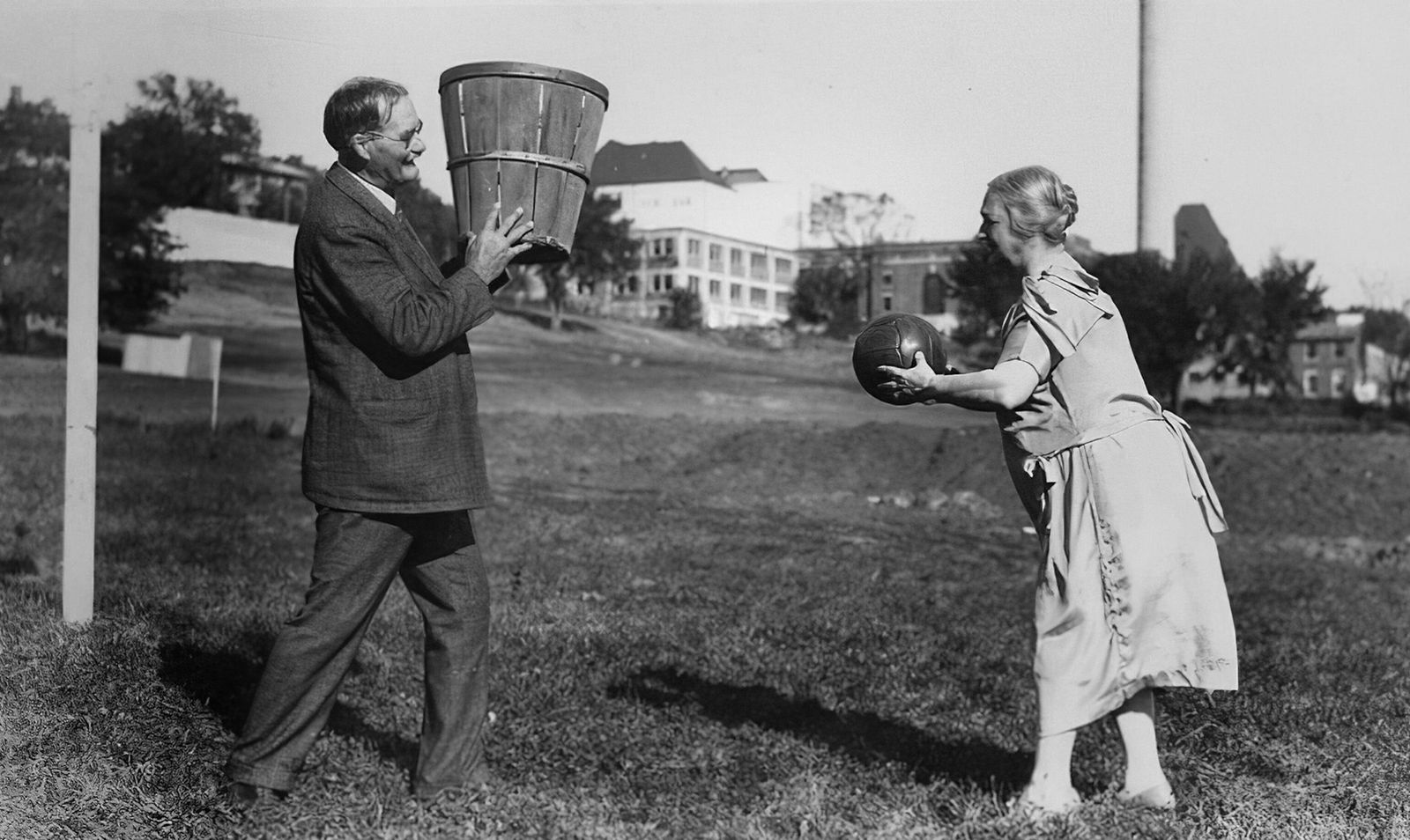 Two people play catch with a ball and bucket outdoors.