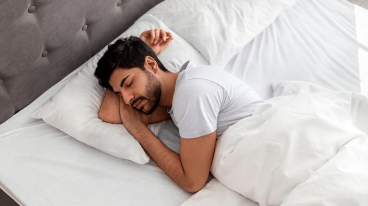 Man sleeping peacefully on a white bed with pillows.