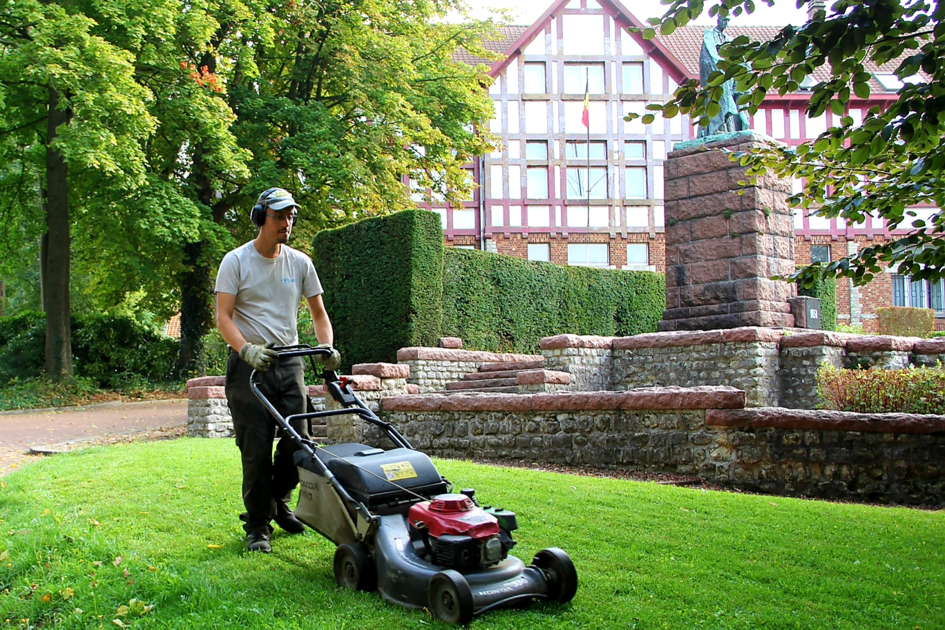 Man mowing a lawn in front of a building and monument.