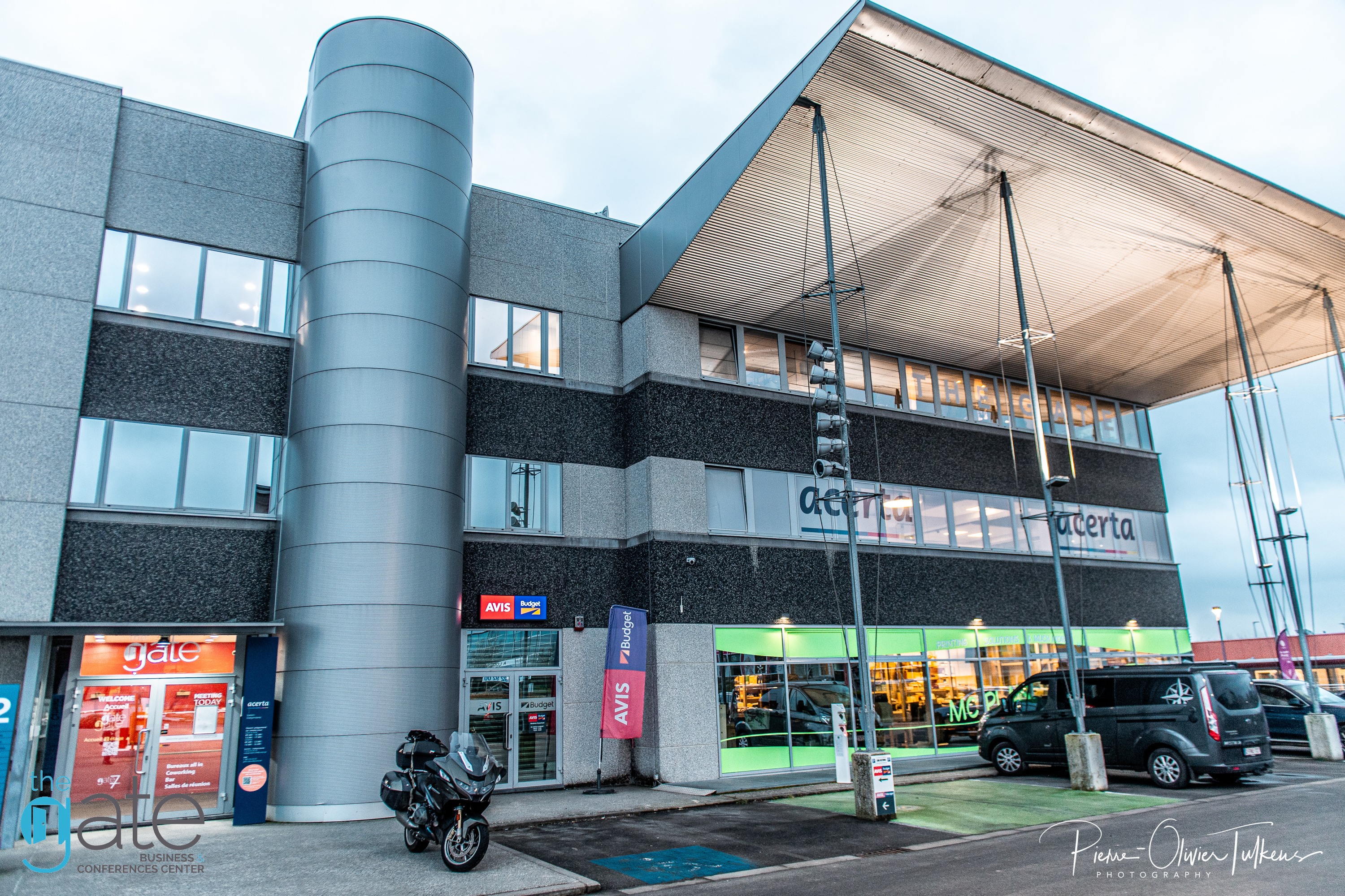 Modern building with large windows and parking area visible.