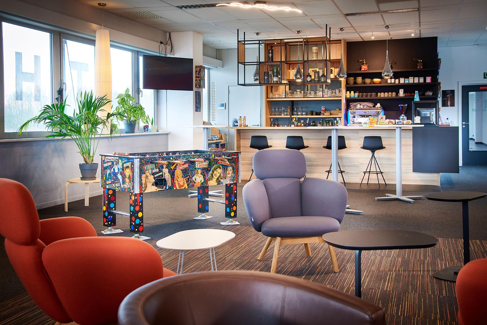 A modern lounge area with colorful furniture and a foosball table.