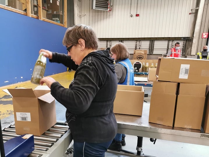 Workers packing bottles into boxes on a conveyor belt.