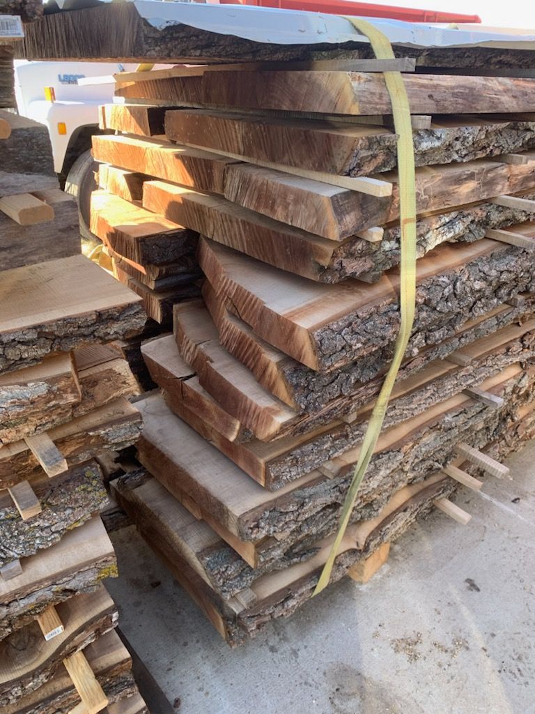 Stacked wooden planks with rough edges, sunlit outdoor setting.