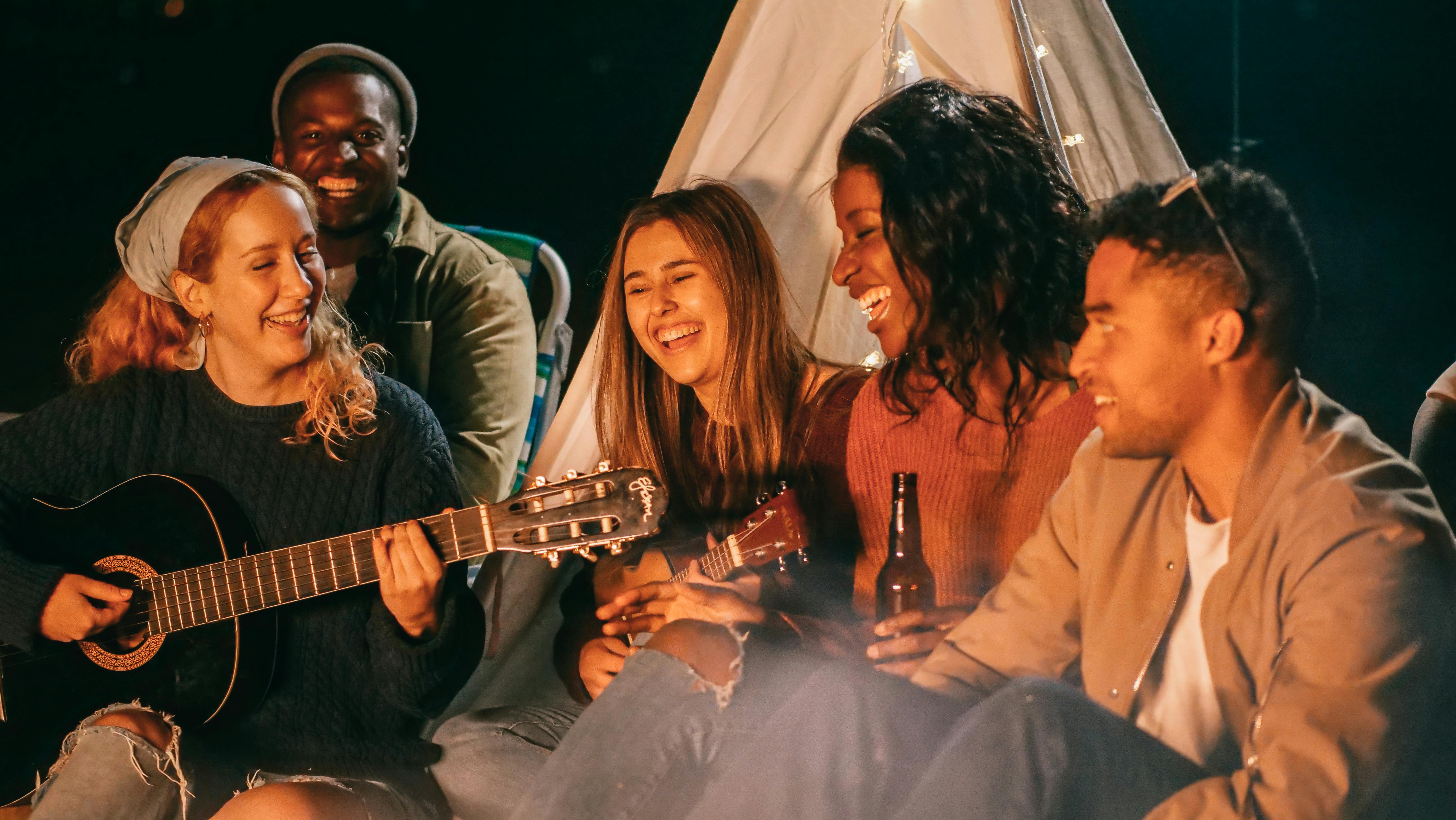 Diverse group of young adults outside with a woman playing guitar