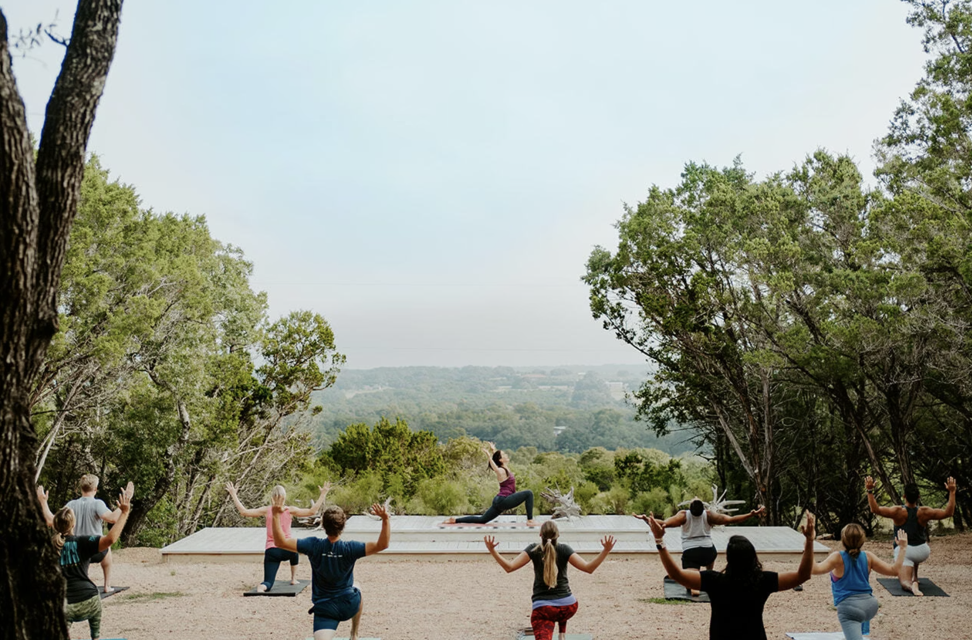 Group practicing yoga outdoors with a scenic view of rolling hills.